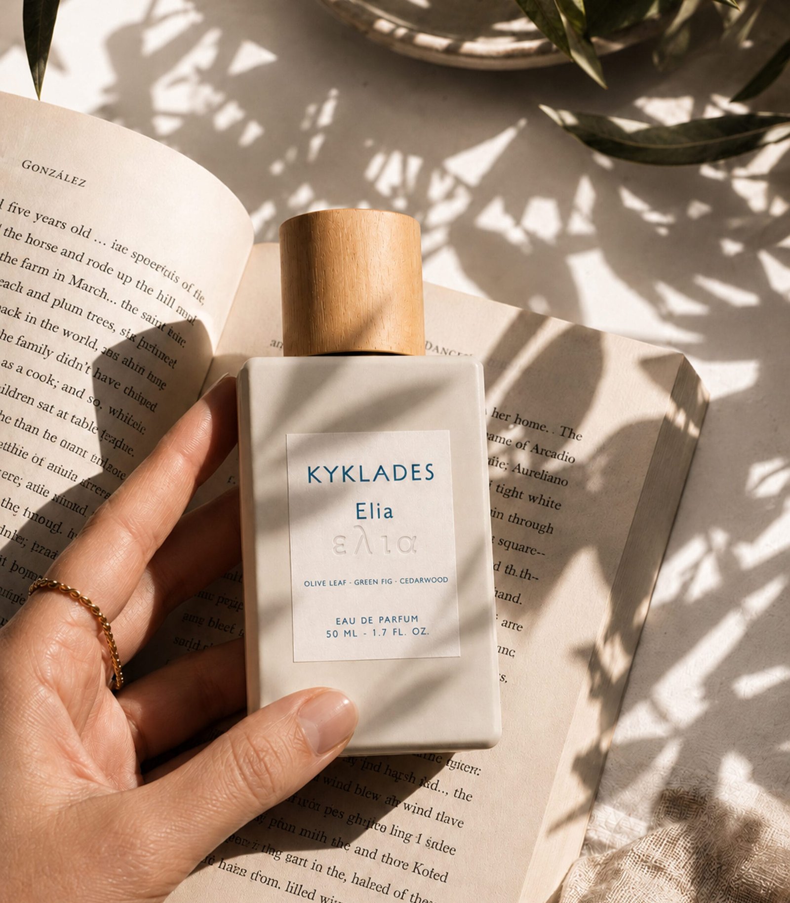 KYKLADES Elia perfume on an open book with natural olive leaf shadows